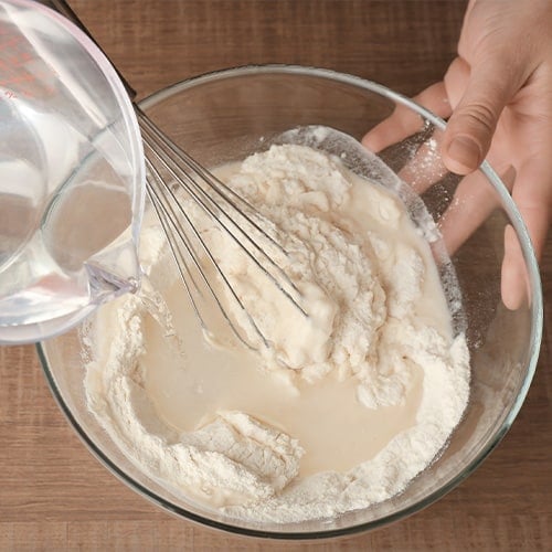 Water being poured into flour to make dough