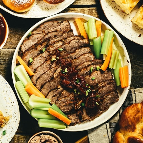 A brisket on a plate with carrots and celery.