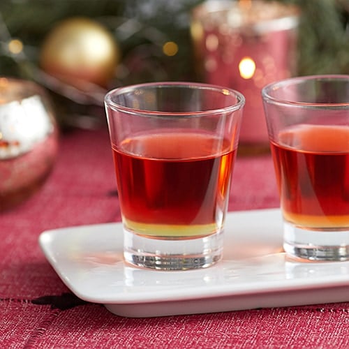 Two red shot glasses with a red drink called Cinnamon Candy Apple.