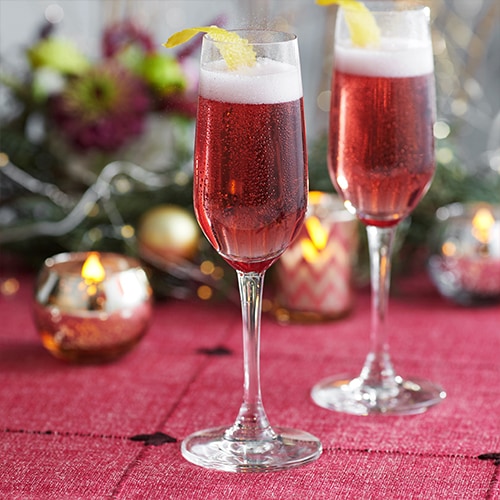 Two champagne glasses with a red drink and lemon twist called a Chambord Kiss Royale.