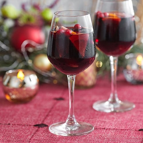 Two glasses of a dark red drink with slices of fruit, cranberries, and cinnamon stick.