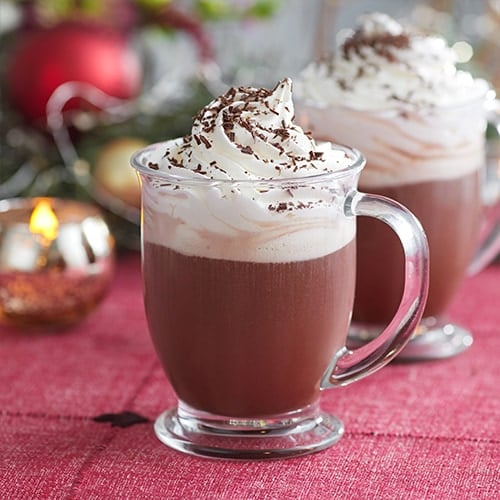 Two glass mugs with Whipped Caramel Hot Cocoa topped with whipped cream and shaved dark chocolate.