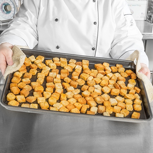 chef holding full size baking sheet with tater tots