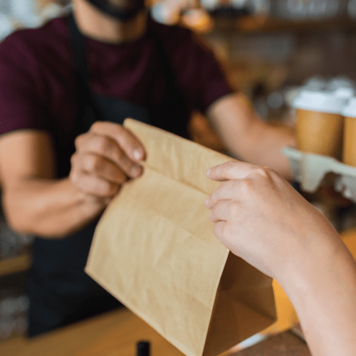 restaurant employee handing over a takeout bag and drink carrier to a customer