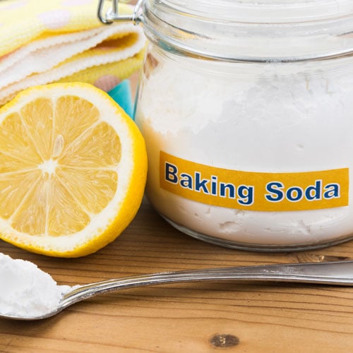 A glass jar of baking soda and half of a lemon.
