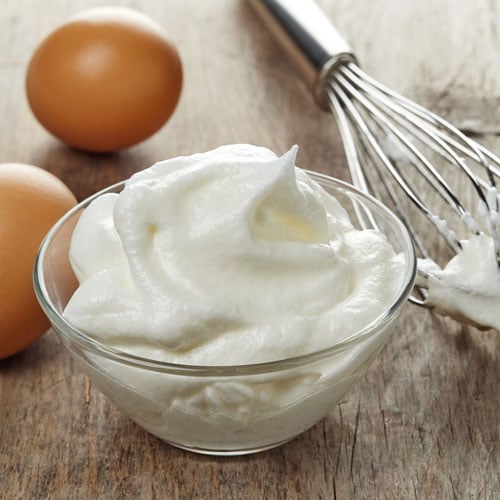 A bowl of whipped eggs and a whisk next to a couple of brown eggs on a countertop.