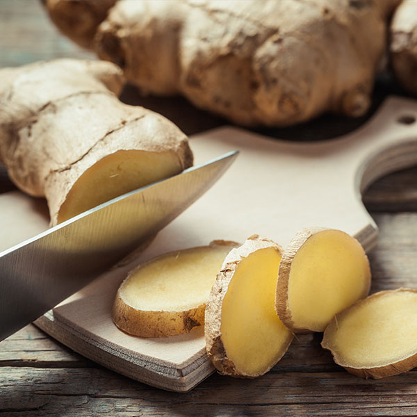 ginger root being sliced by a knife on a cutting board