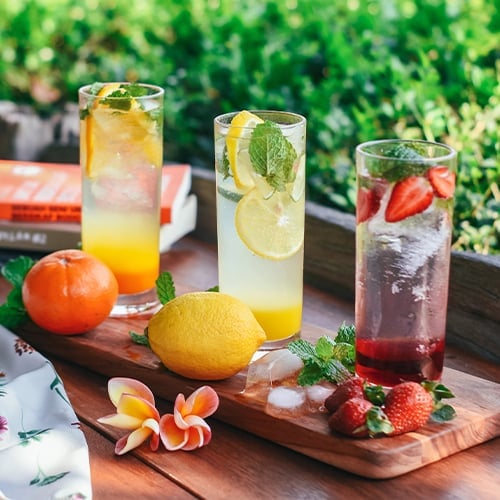 3 glasses of hard seltzer on an outdoor bar surface with various fruit garnishes