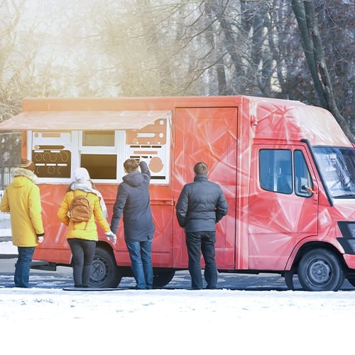Four people standing near and ordering at red food truck in winter