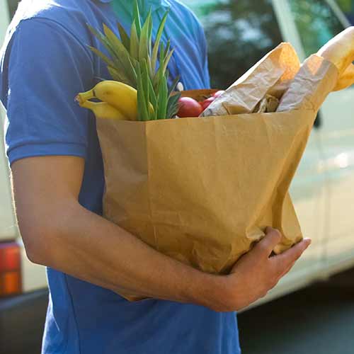 delivery worker holding grocery bag with fresh produce and bread