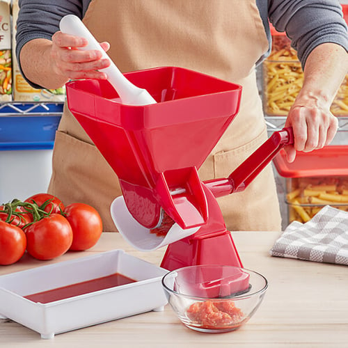 chef using a manual red tomato juicer to make tomato sauce