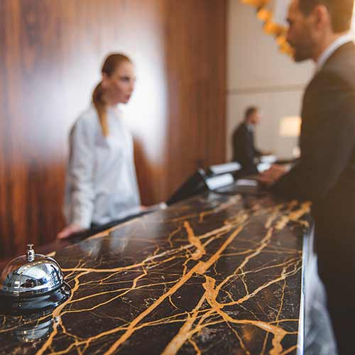 A guest at the registration desk with a Guest Services worker with small stainless steel bell on the counter.