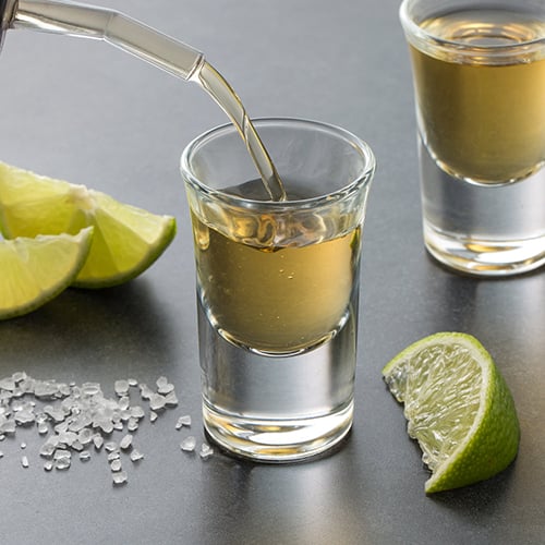 shot of tequila being poured with salt and limes in background