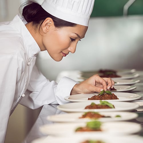 concentrated female chef garnishing food in kitchen