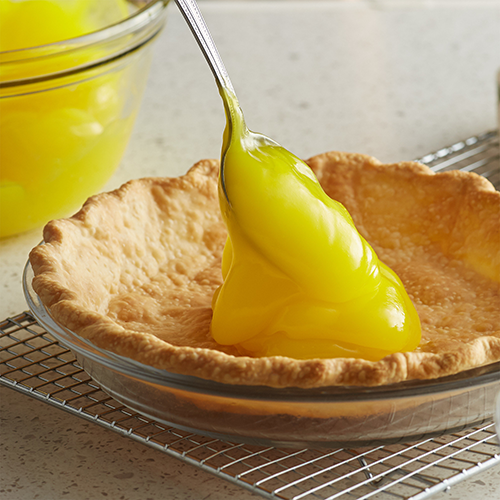 spooning lemon custard into baked pie crust