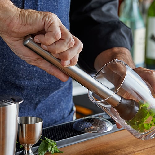 male bartender muddling mint in glass at side angle