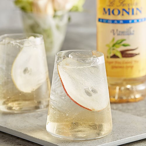 chilled cocktail glass filled with fizzy vanilla flavored drink with slice of apple and ice