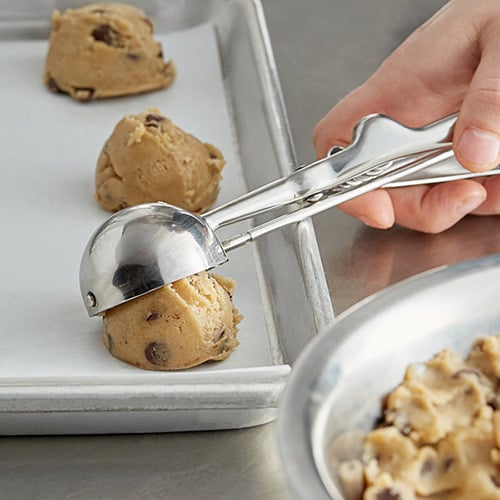 person using a a size 20-36 cookie scoop to drop medium sized scoops of cookie dough on a sheet with parchment paper