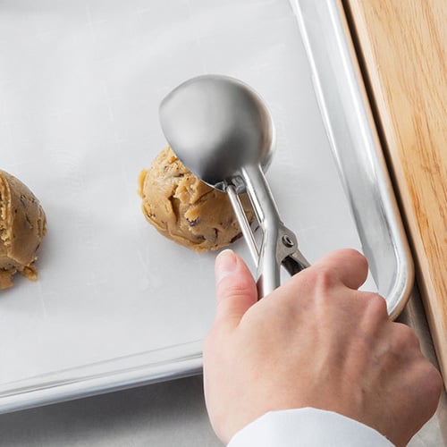 person using a cookie scoop to drop cookie dough on sheet with parchment paper