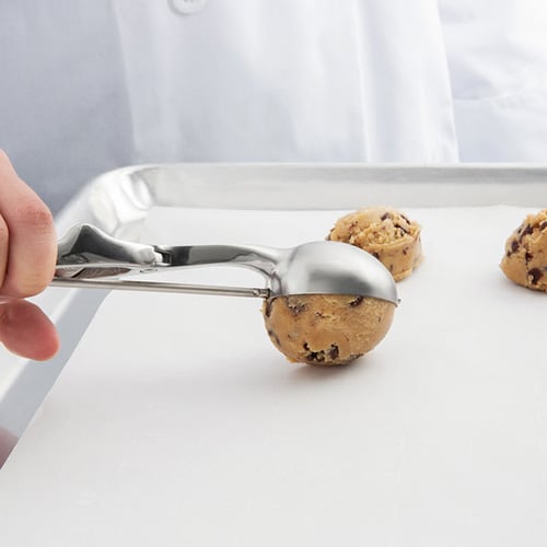 out of frame hand using a cookie scoop to drop cookie dough on a sheet with parchment paper