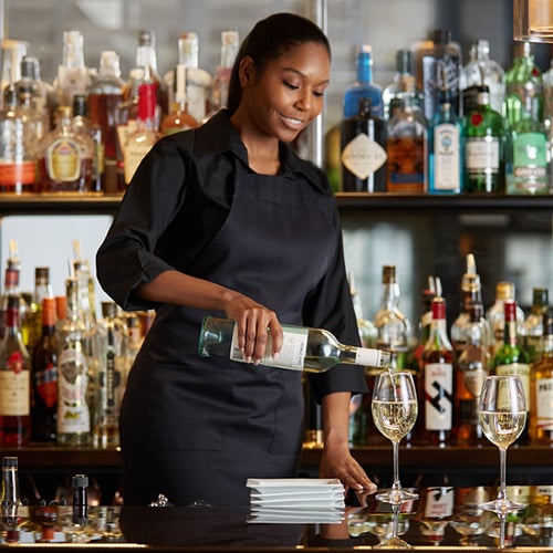 female bartender at upscale restaurant pouring white wine from bottle into glass