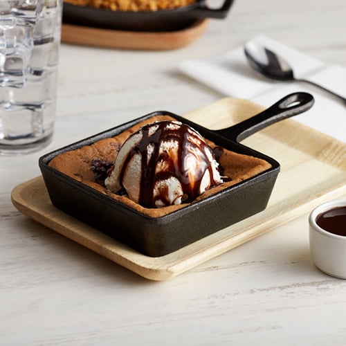 cookie in a mini cast iron square server skillet with a scoop of ice cream and chocolate syrup on top