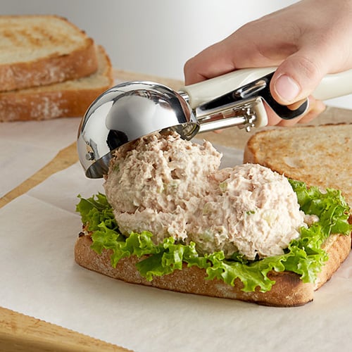 person scooping tuna onto a piece of bread with lettuce