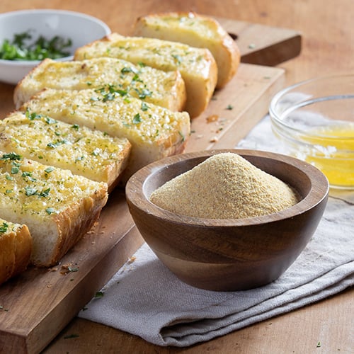 Granulated garlic in wooden dish with garlic bread in background