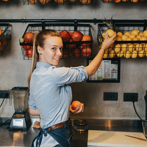 happy young female bartender standing at juice bar counter