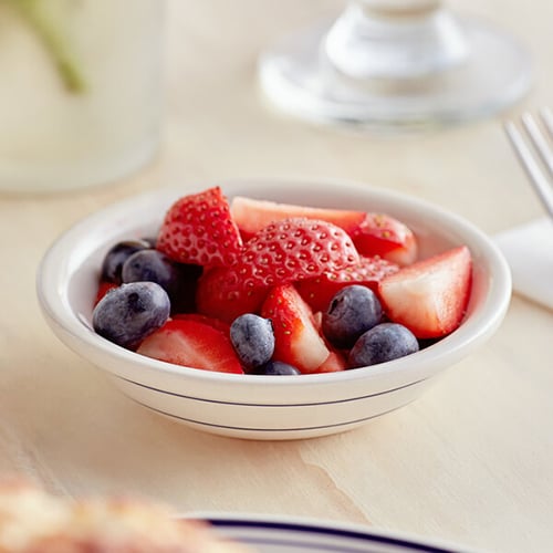 monkey dish with blueberries and sliced strawberries on wooden table