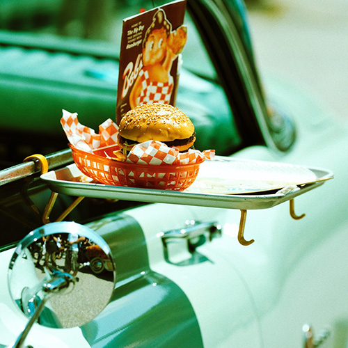 tray with a burger in a red plastic basket hooked on the side of an antique car window