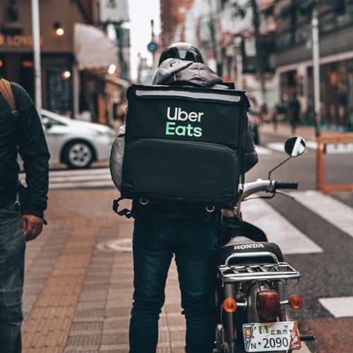 uber eats driver carrying an insulated food carrier getting on a motorcycle
