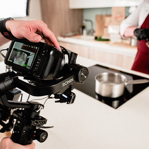 videographer holds a ronin camera pointed at a stainless steel pot with chef in background