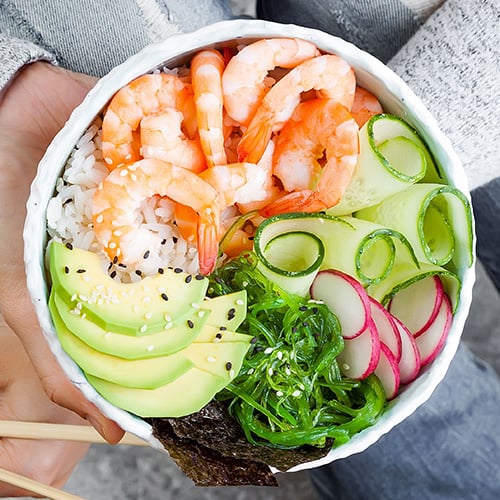 girl wearing jeans holding shrimp poke bowl with seaweed, avocado, cucumber, radish
