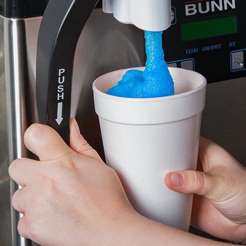 close up of hands pouring a blue raspberry slushie into a styrofoam cup