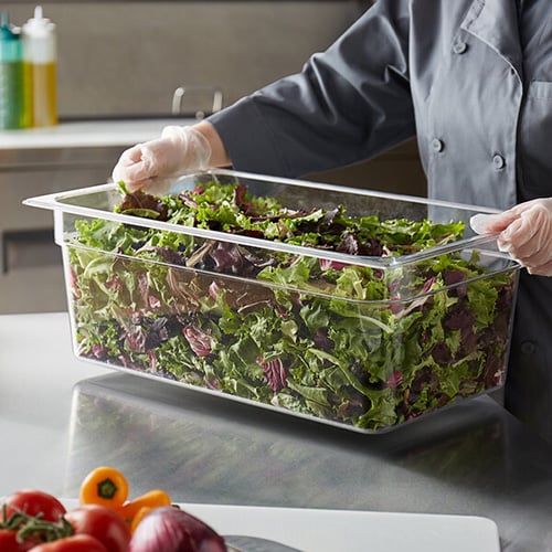 mixed greens in plastic container on stainless steel work table
