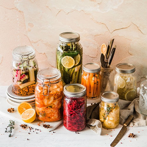 Bottles with homemade red juice and jars of various pickled