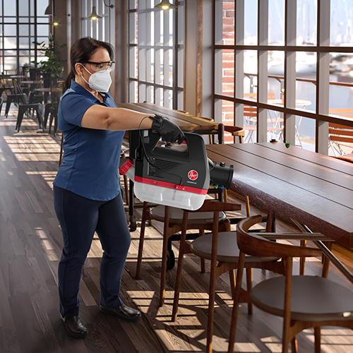 female employee using an electrostatic sprayer to sanitize restaurant table