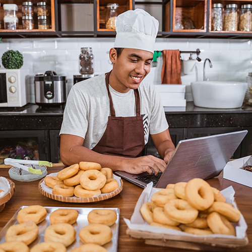 chef using laptop to sell homemade donuts made in home kitchen
