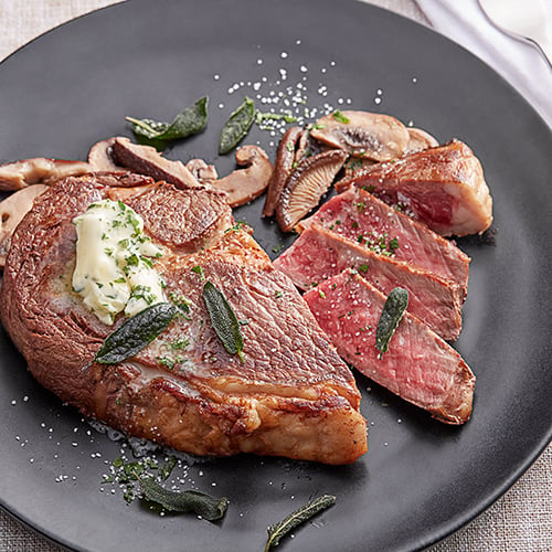 dry aged beef with sauteed mushrooms topped with butter on black slate plate