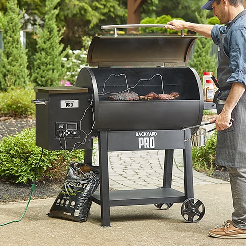 man with apron and hat smoking barbecue on backyard pro smoker outside