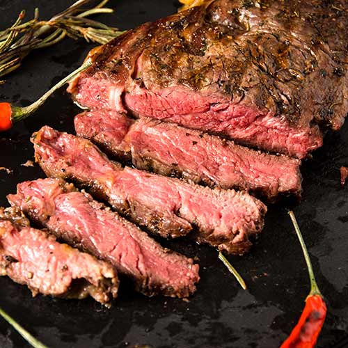 rare steak on black rectangular plate with rosemary