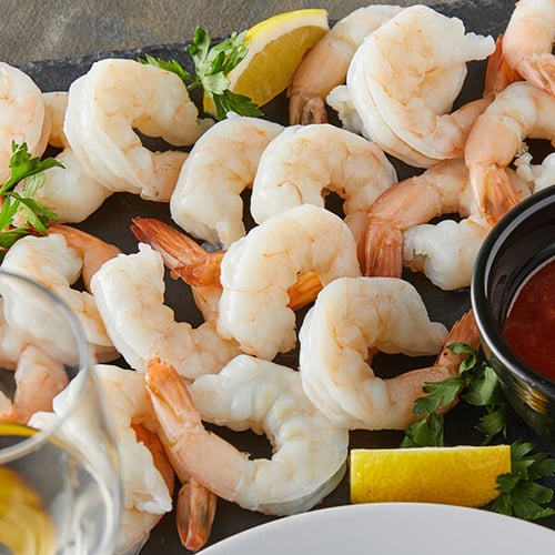 shrimp cocktail on black slate serving board with lemons on the side