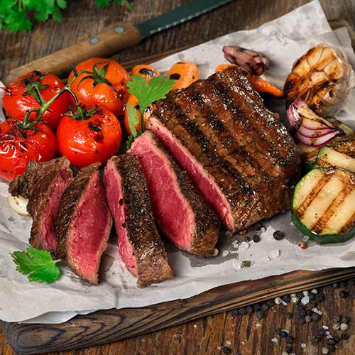 sliced steak with grilled vegetables on wooden background