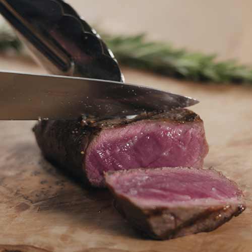 slicing blue filet mignon steak on wood board