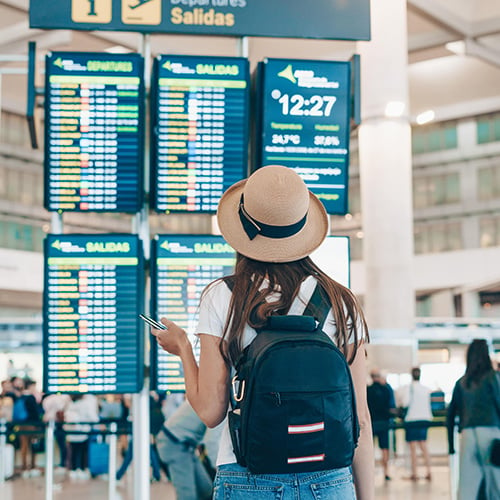 woman with backpack and hat at airport looking at departure times on board