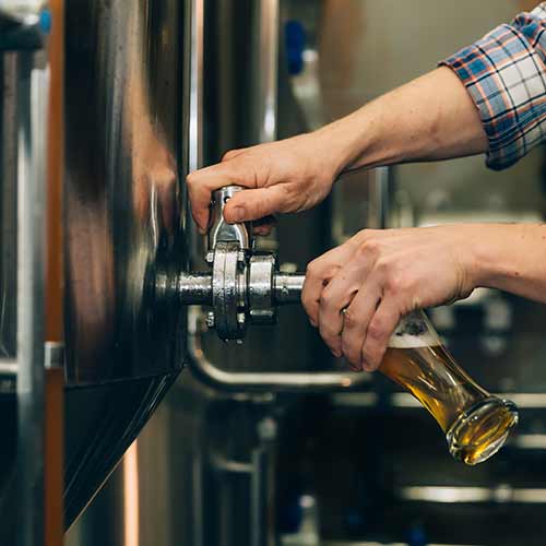 brewer filling beer in glass from tank at brewery