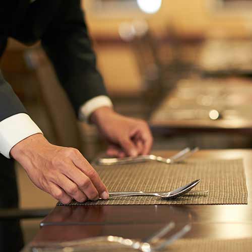 hands of hotel waiter arranging silverware on napkin on table