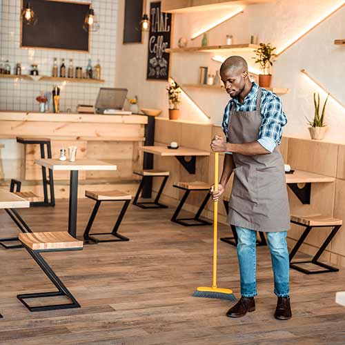 employee sweeping with broom in coffee shop