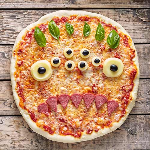 monster zombie pizza snack face with mozzarella basil and sausage on vintage wooden table
